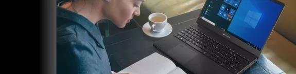 Woman at desk writing in notepad with coffee and laptop