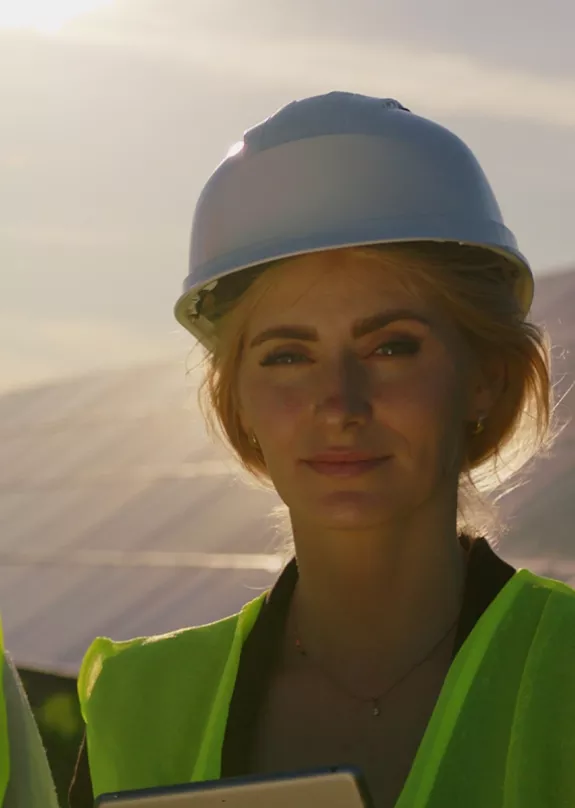woman and man wearing hard hats standing in front of PV plant at sunset